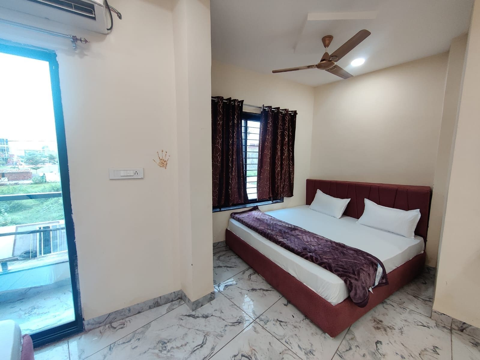 A bedroom with a bed, a ceiling fan, a window with curtains, and a view of the outside.