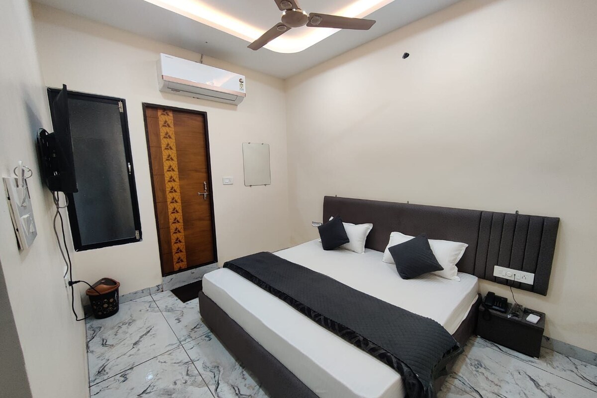 Quarto com cama, ventilador de teto, ar condicionado, porta e TV fixada na parede.