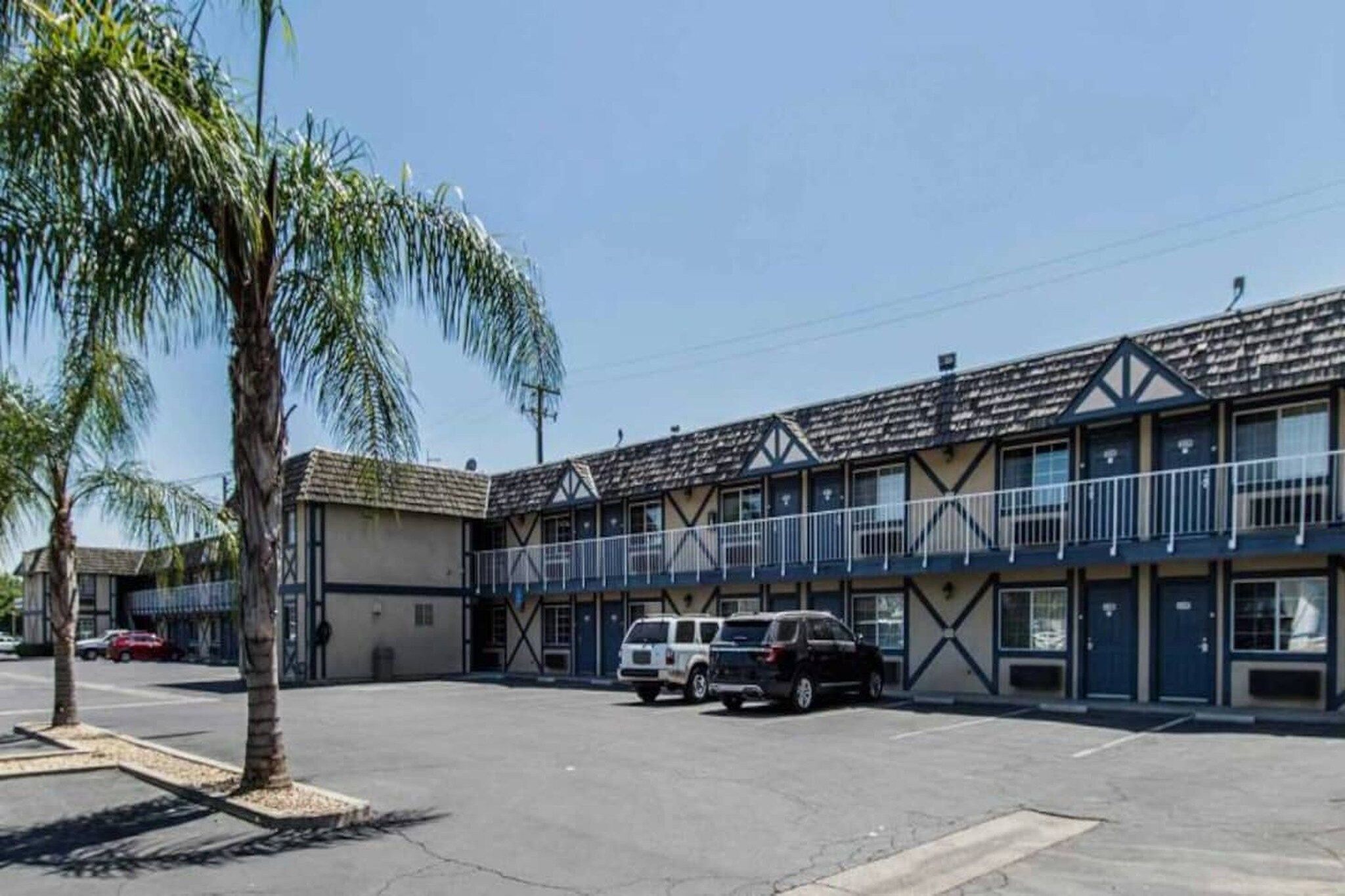 A motel with a parking lot, two-story buildings, and a palm tree.