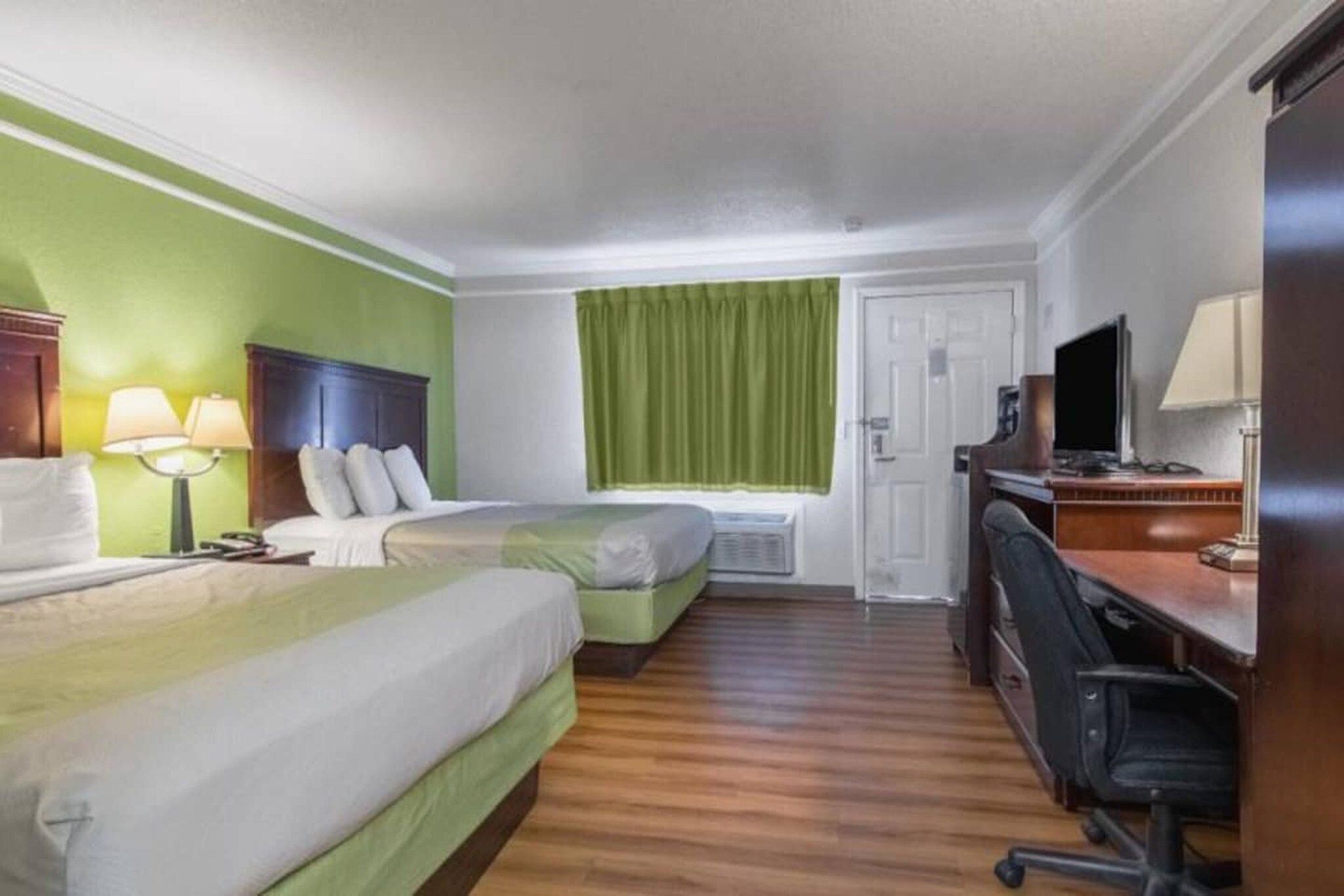 Habitación de hotel con dos camas, un escritorio con silla, televisor y ventana con cortinas.