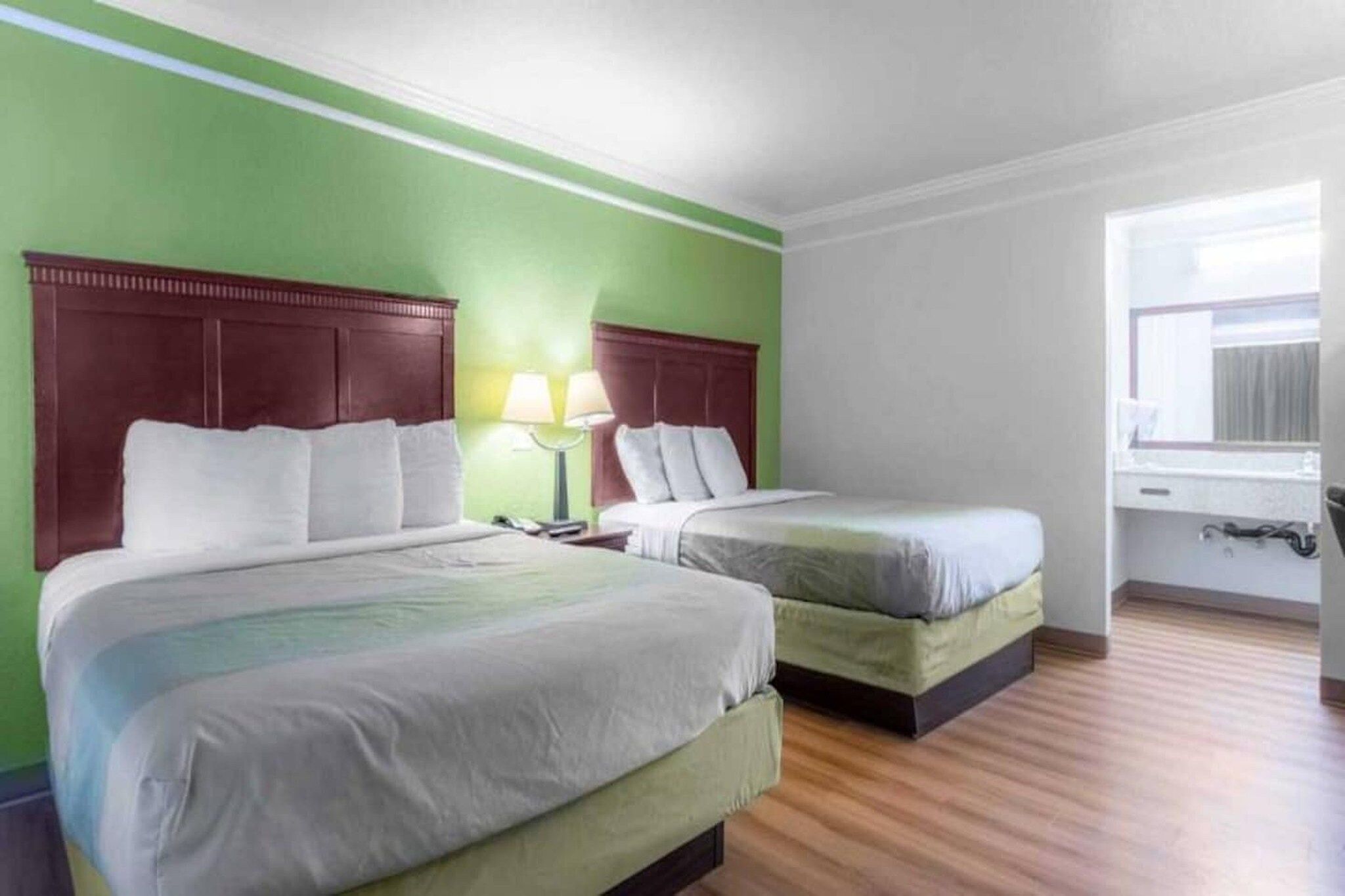 Habitación de hotel con dos camas, una mesita de noche, una lámpara y un ventanal.