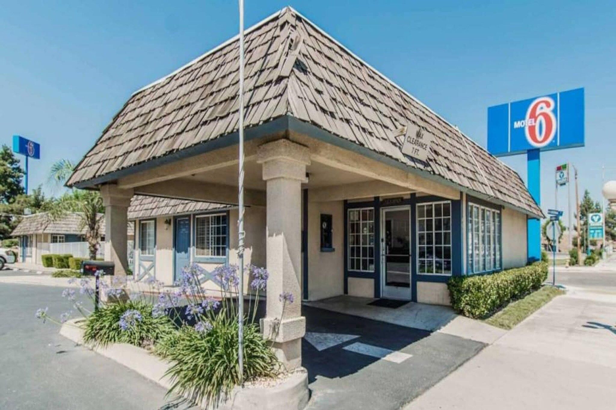 Un motel con una estructura de un solo piso, un acceso cubierto y un cielo azul despejado al fondo.