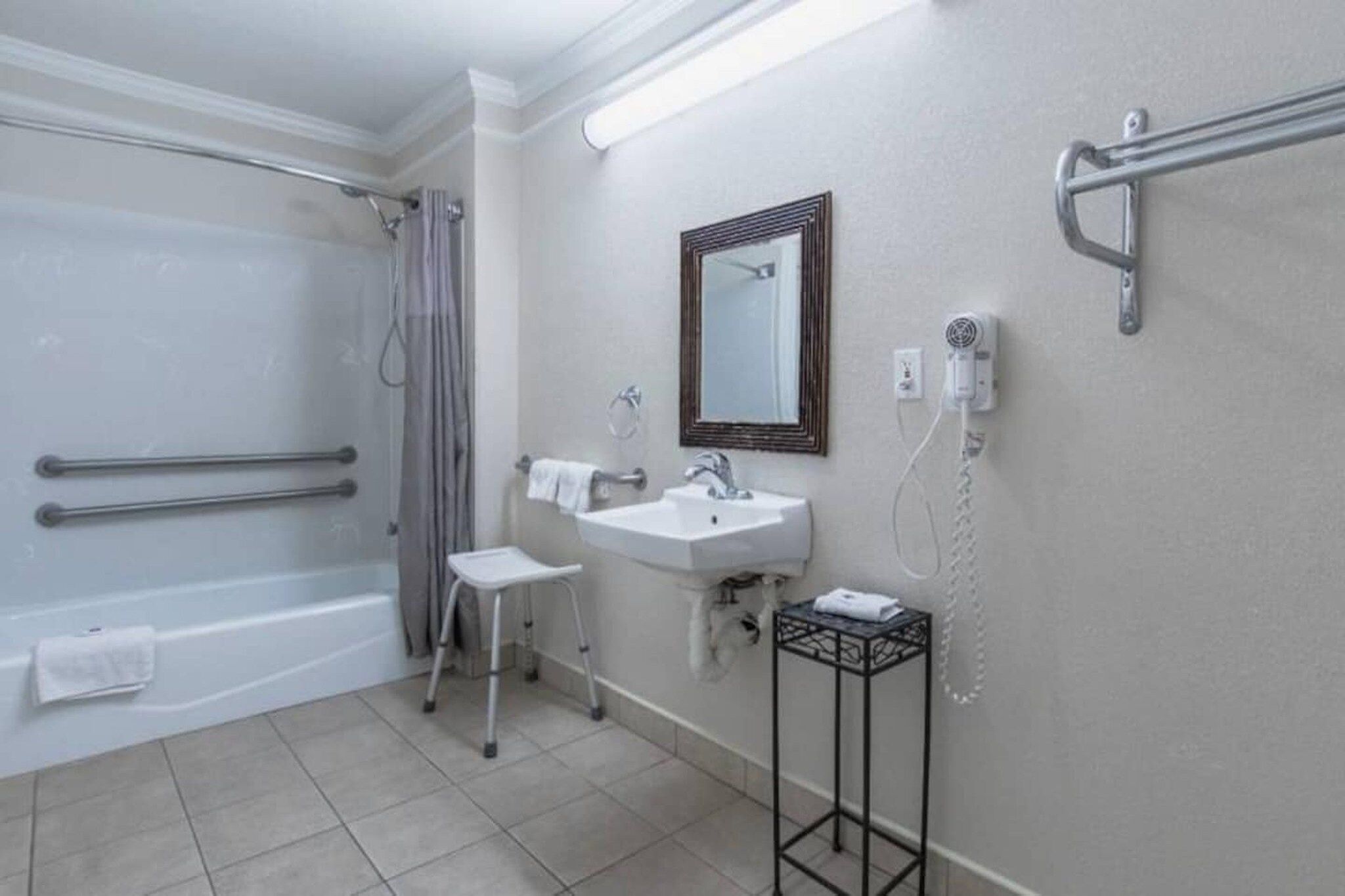 Ein Badezimmer mit einer Badewanne, einem Waschbecken, einem Spiegel, einem Handtuchhalter und einem Händetrockner.