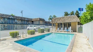 A swimming pool with a fenced area, lounge chairs, and a building with a tiled roof. - Cozy Studio 1 Queen Bed|Free Wifi (Kingsburg)
