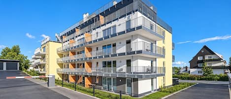 Un immeuble résidentiel à plusieurs étages, doté de balcons, d’une allée d’accès fermée par un portail et surplombant un ciel dégagé.