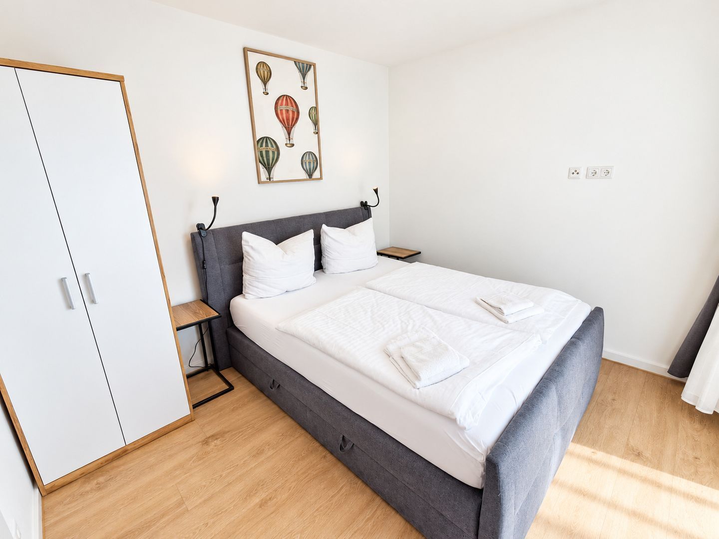A neatly arranged bedroom with a bed, bedside tables, and a wardrobe.