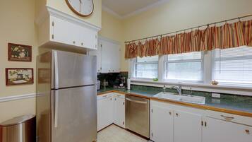 Una cocina con armarios blancos, un refrigerador de acero inoxidable, una ventana con persianas y un reloj en la pared.