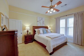 Un dormitorio con cama, mesitas de noche, ventilador de techo y ventana con cortinas.