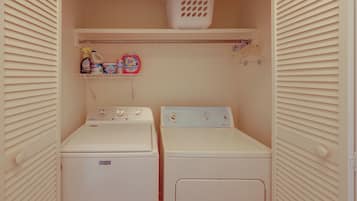 Un cuarto de lavandería con dos lavadoras y secadoras Maytag, un estante con productos de limpieza y una cesta de ropa.