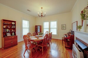 A dining room with a wooden table, chairs, a chandelier, and a piano.