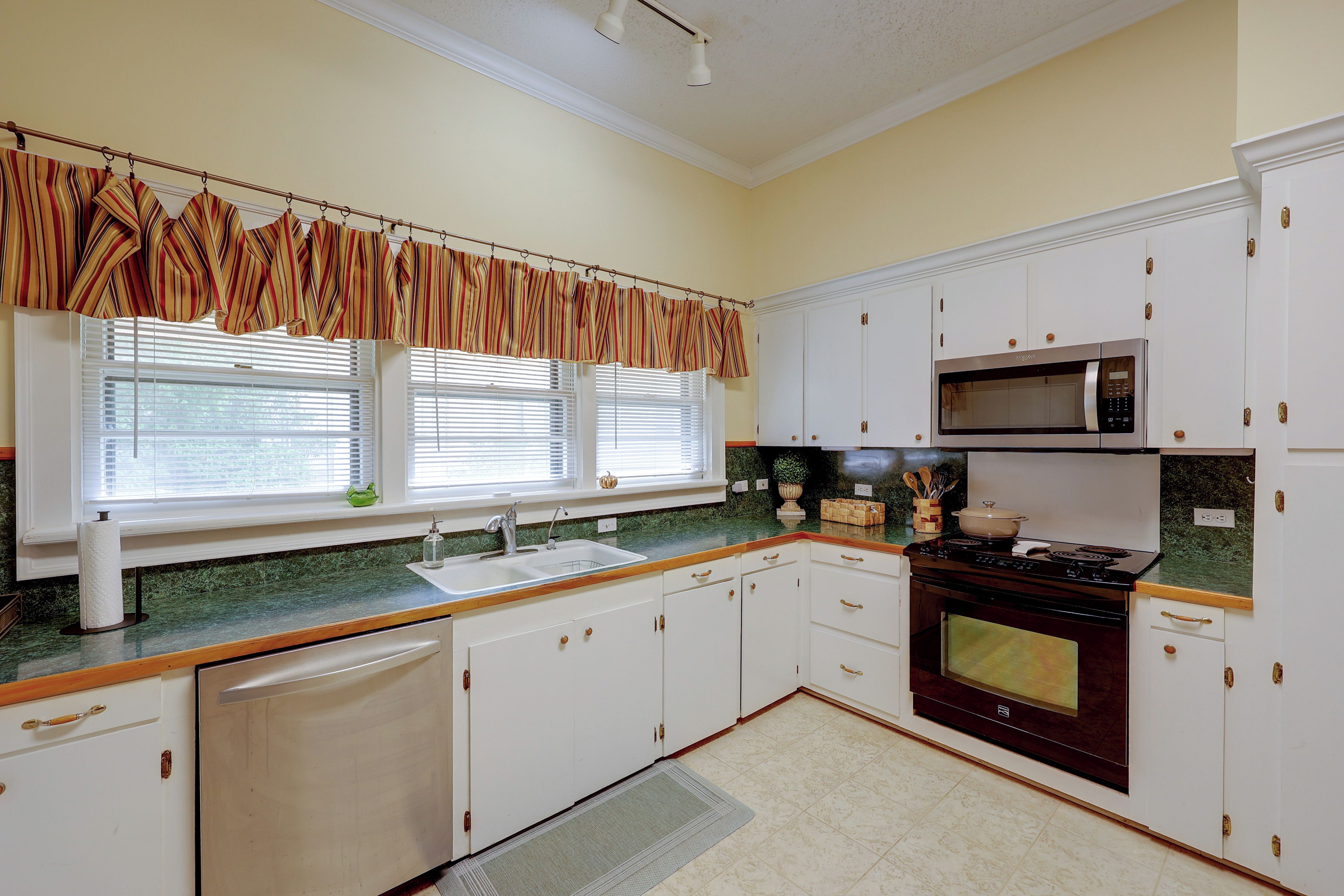 Una cocina con armarios blancos, microondas, estufa y ventana con persianas.