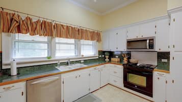 Una cocina con armarios blancos, microondas, estufa y ventana con persianas.