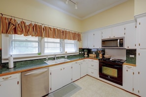 A kitchen with white cabinets, a microwave, a stove, and a window with blinds.