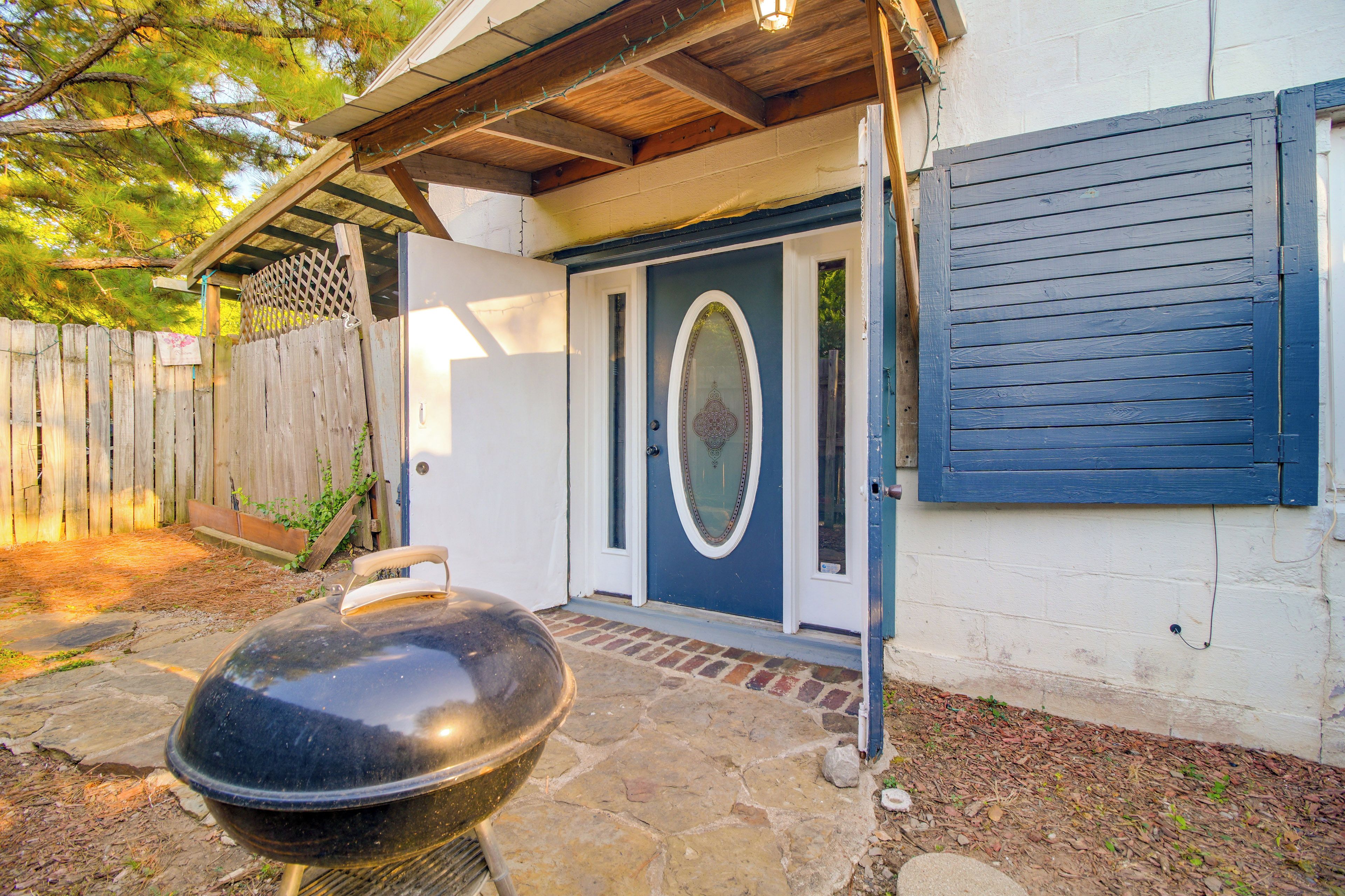 A barbecue grill in front of a house with a blue door and a wooden fence.
