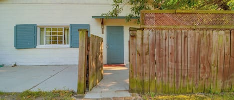 Una casa de un piso con puerta principal, ventana con contraventanas y cerca de madera.