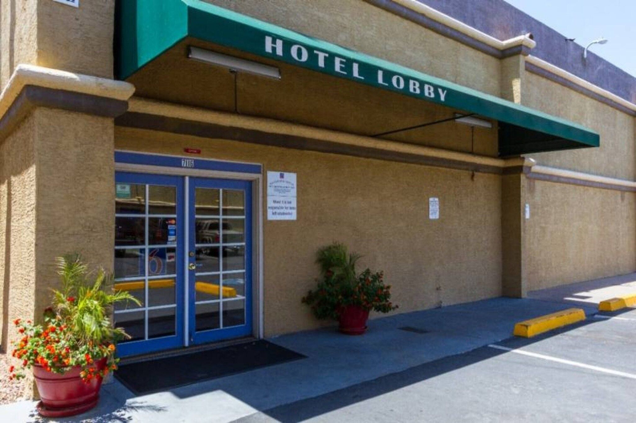 A hotel lobby with a blue entrance door, a green awning, and potted plants.