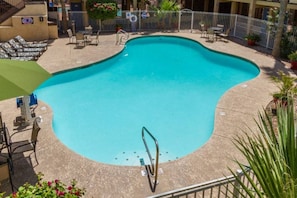 A swimming pool with a diving board, surrounded by lounge chairs and tables, and a fenced area with potted plants.