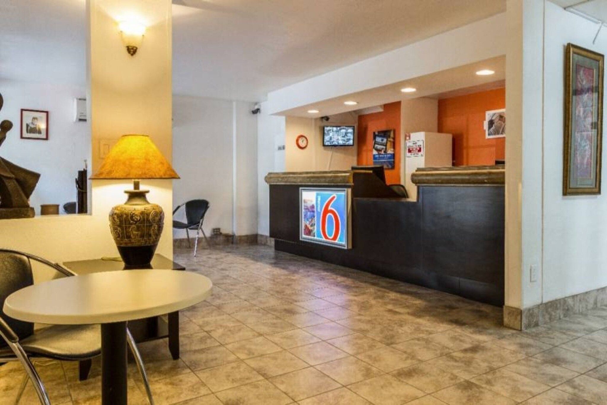 A hotel reception area with a reception desk, a television, a clock, and a table with chairs.