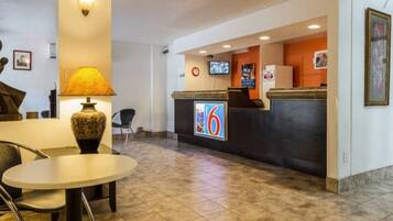 A hotel reception area with a reception desk, a television, a clock, and a table with chairs.