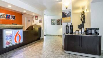 A hotel lobby with a reception desk, a large number '6' sign, a coffee station, and a statue.