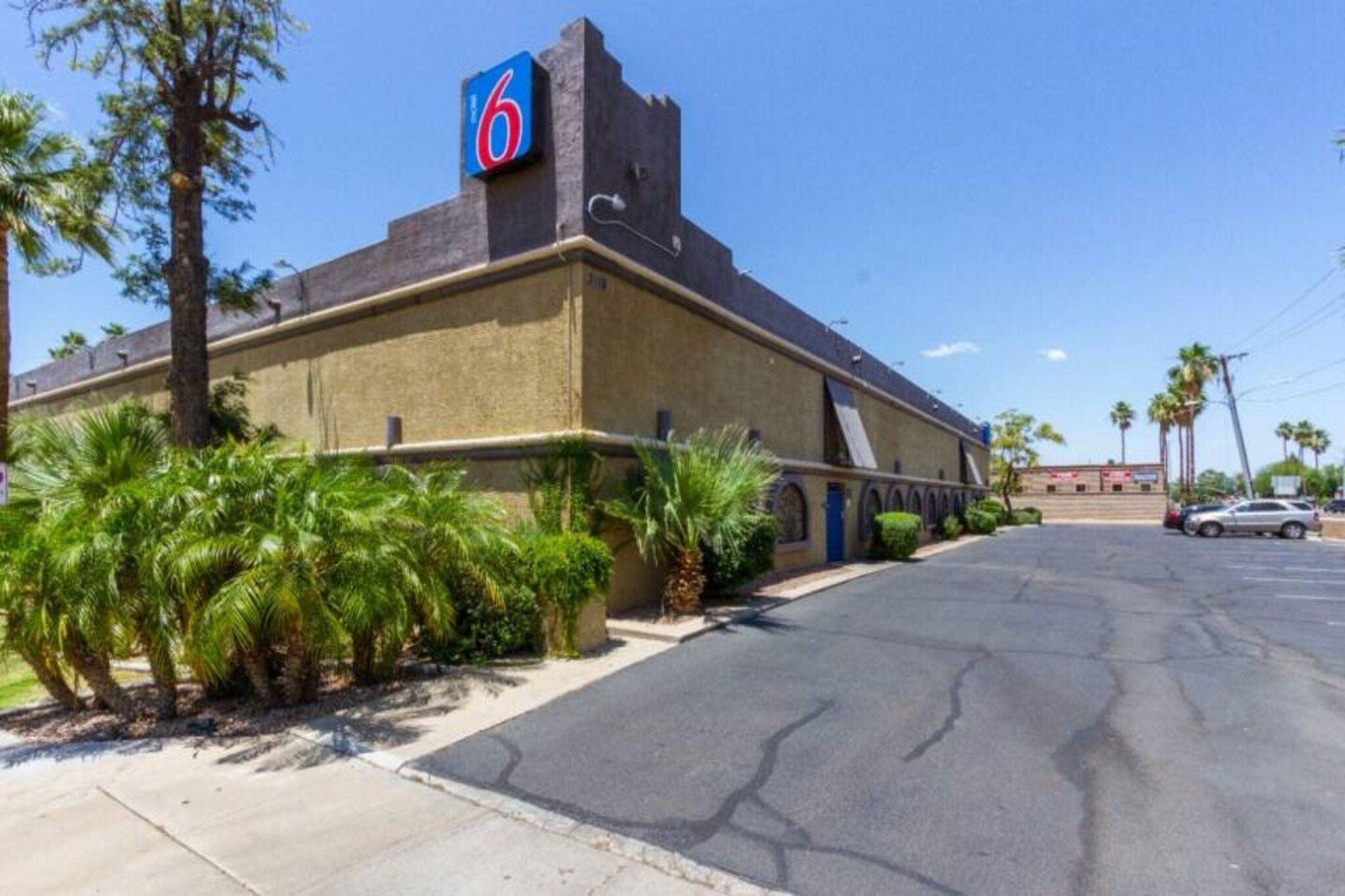 A motel with a prominent '6' sign, a parking lot, and palm trees.