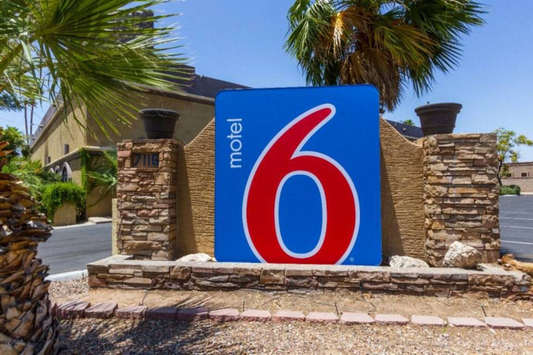 A motel sign with the number 6, surrounded by stone pillars and palm trees.