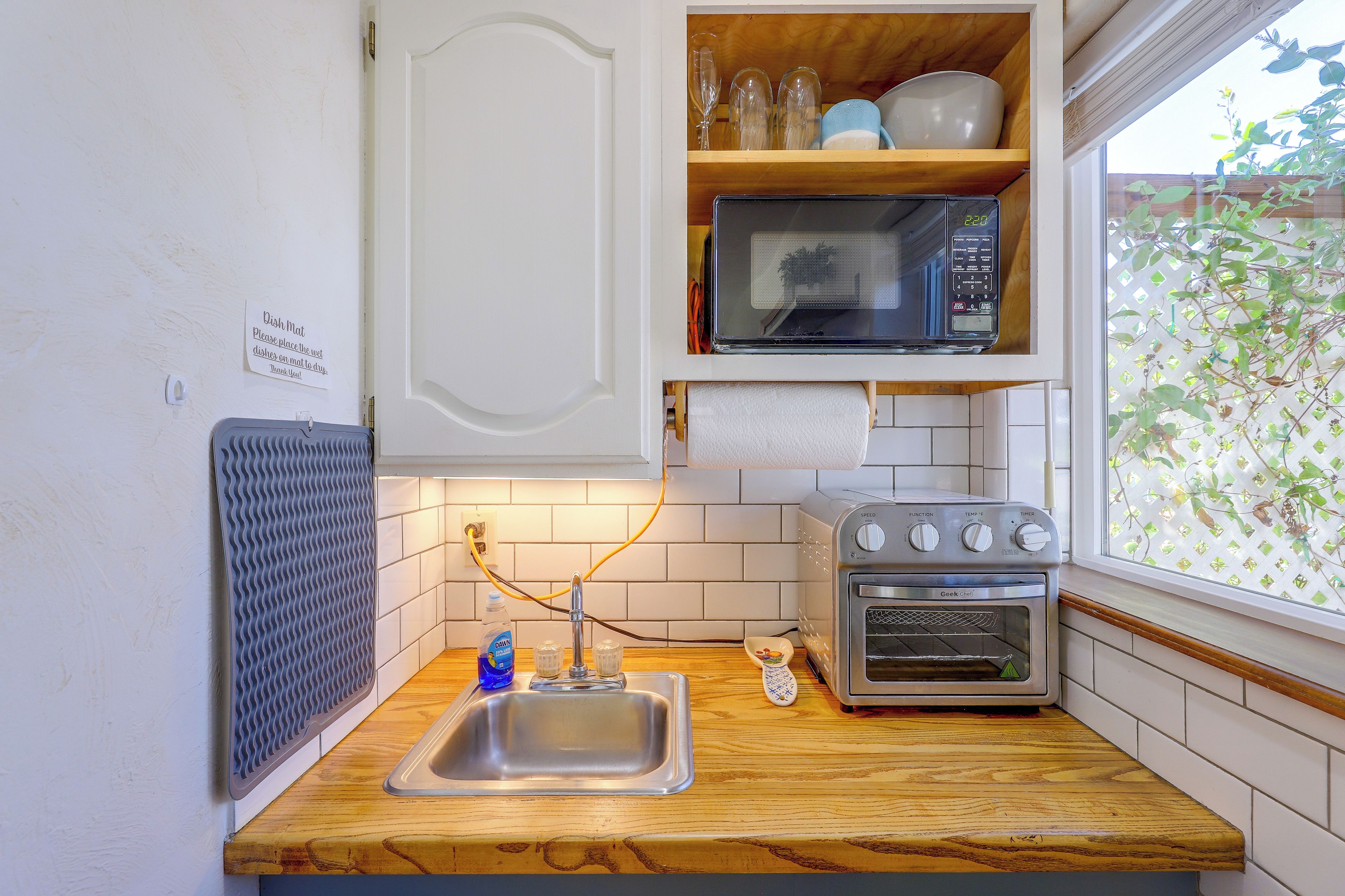 Una cucina compatta con forno a microonde, forno tostapane e un cartello con la scritta "stuoia per piatti" appeso al muro.