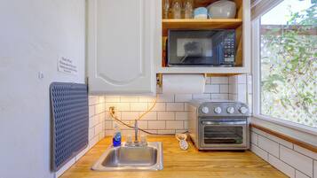 Una cucina compatta con forno a microonde, forno tostapane e un cartello con la scritta "stuoia per piatti" appeso al muro.