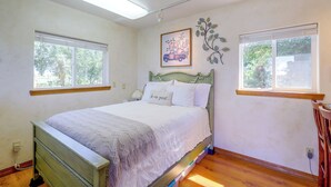 Ein Schlafzimmer mit einem Bett, zwei Fenstern, einem Wandbild und einer Heizung.