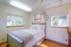 Un dormitorio con cama, dos ventanas, un cuadro colgado en la pared y un radiador.