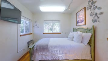 A bedroom with a bed, two windows, a flat-screen TV, and a wall-mounted artwork.