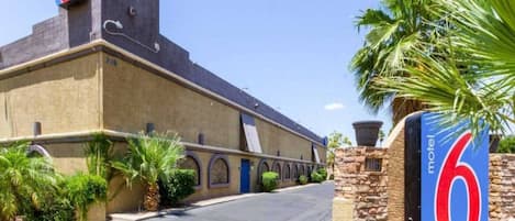 A building with a large '6' sign, a paved road, and palm trees.