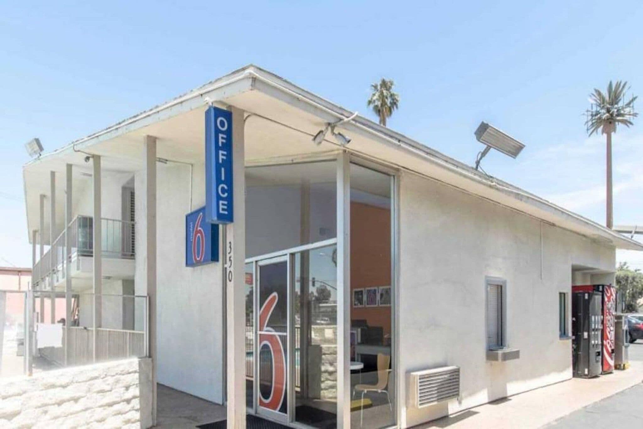 A small building with a sign indicating it's an office, a glass door entrance, and a vending machine outside.