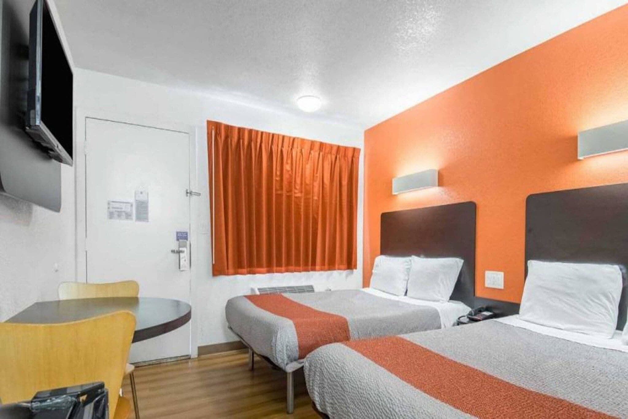 A hotel room with two beds, a desk, a chair, and a television.