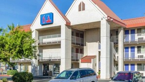 Un hotel con un llamativo letrero azul, varios balcones y un estacionamiento con coches.