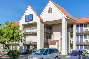 Um hotel com um letreiro azul grande, várias varandas e um estacionamento com carros.