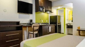 Una habitación de hotel con cama, escritorio, silla, kitchenette y televisor.