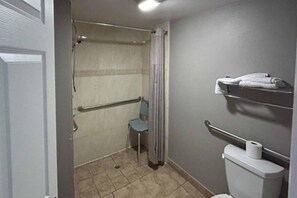 A small bathroom with a shower, a toilet, a handrail, and a towel rack.