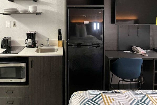 Una kitchenette compacta con microondas, tostadora, cafetera y un lavamanos.
