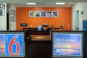 A motel reception desk with a large '6' sign, a digital display, and a sign stating 'We'll leave the light on for you.'