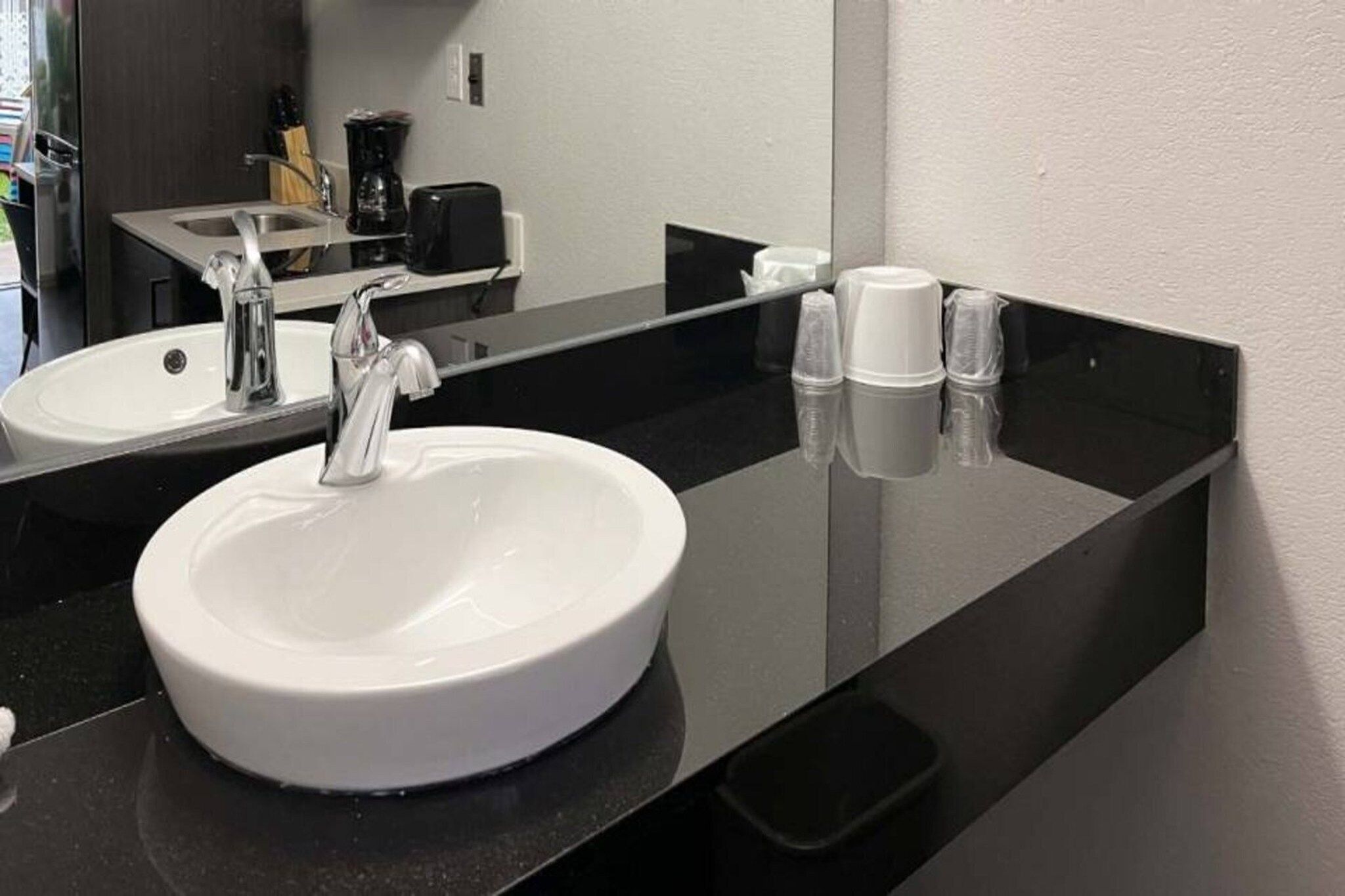 A bathroom with a white sink, a mirror, and a black countertop.