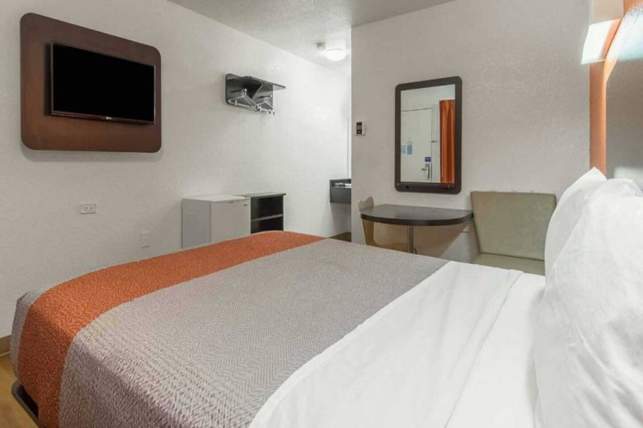 A hotel room with a bed, a desk, a chair, a television, and a mirror.