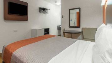 A hotel room with a bed, a desk, a chair, a television, and a mirror.