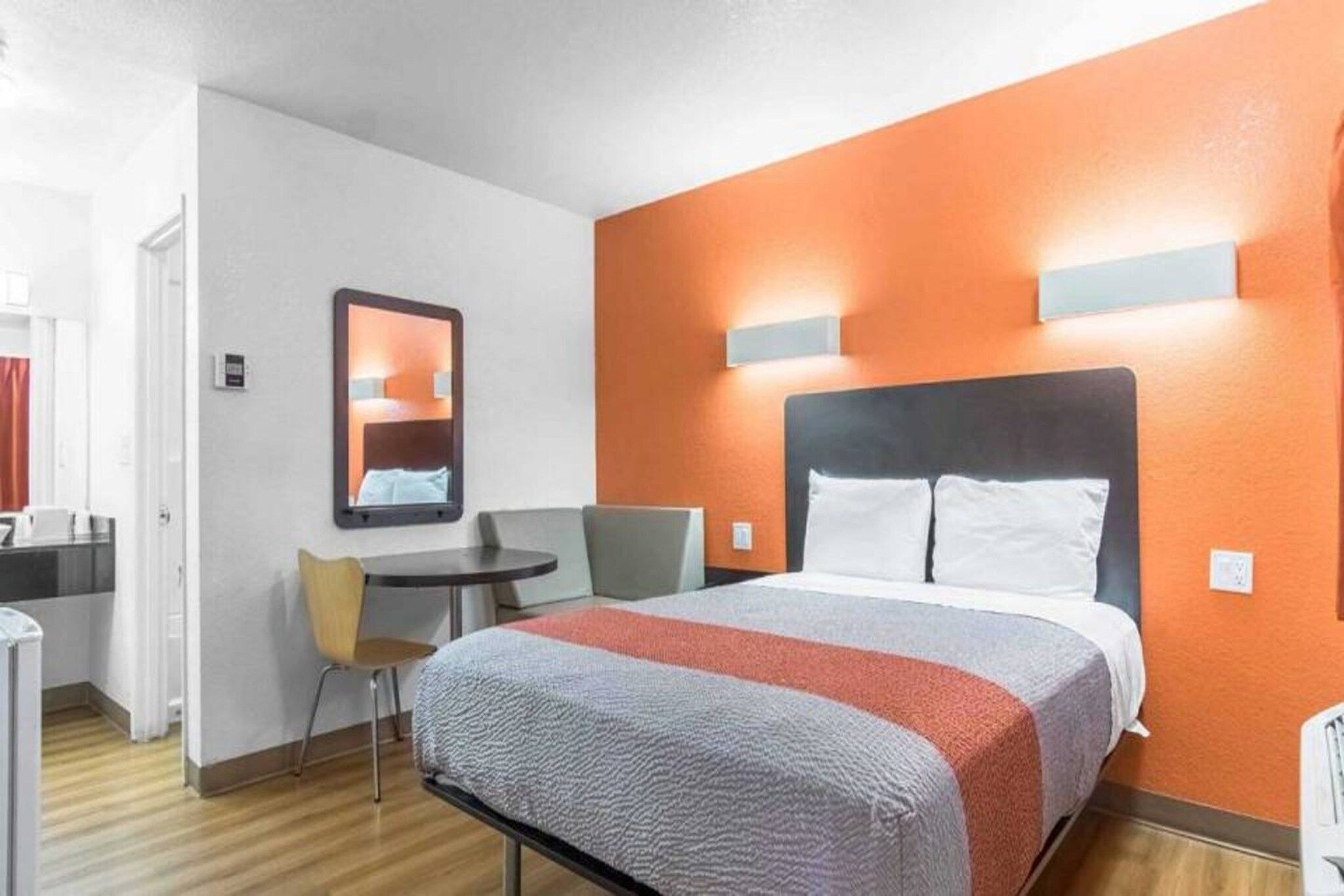 Una habitación de hotel con cama, escritorio, silla y espejo.
