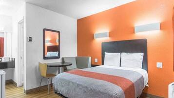 Una habitación de hotel con cama, escritorio, silla y espejo.
