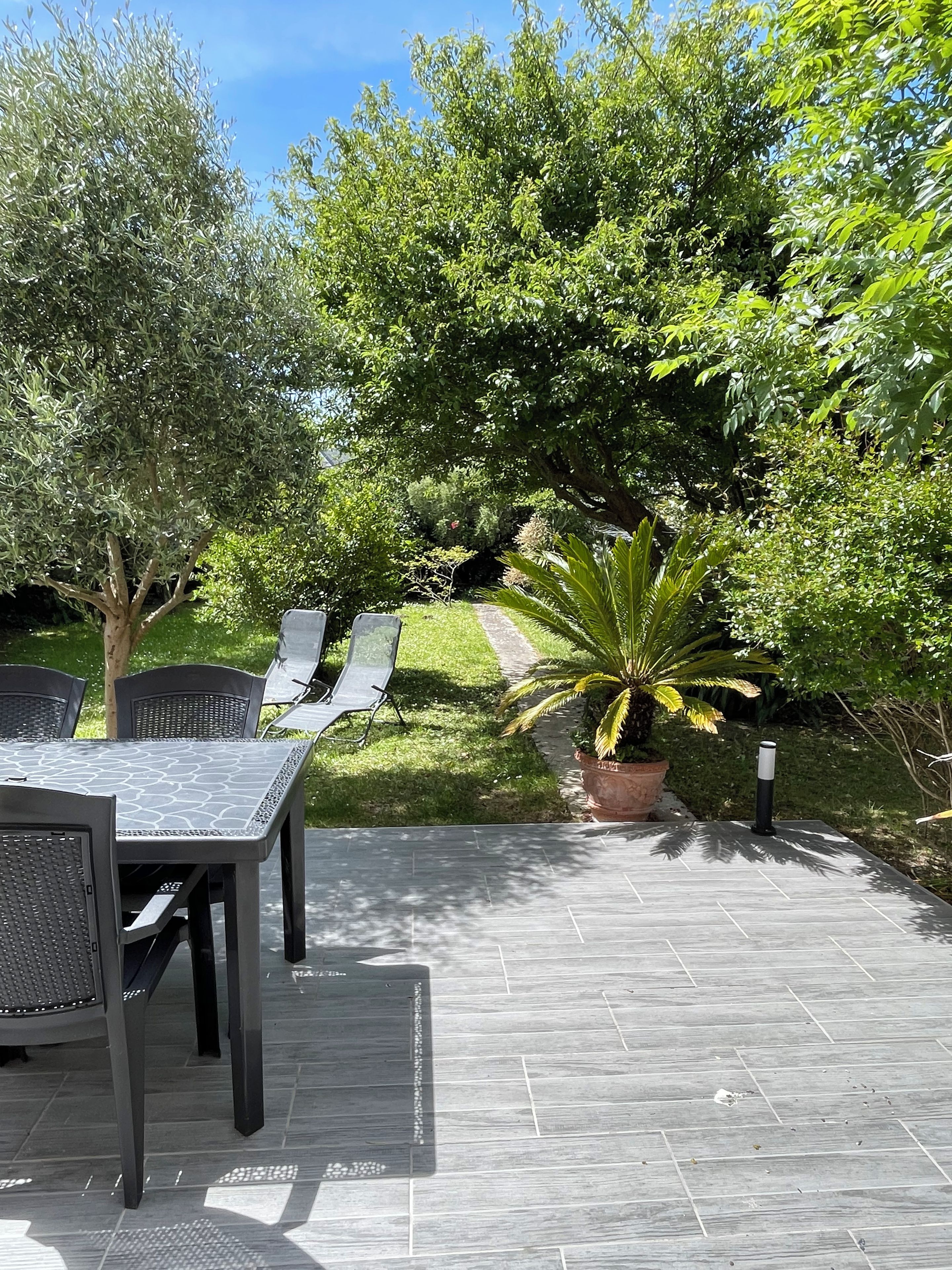 An outdoor patio with a table and chairs, surrounded by greenery and trees.