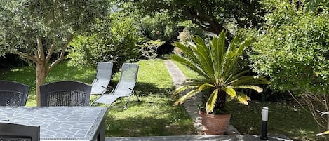 Un patio exterior con una mesa y sillas, rodeado de follaje y árboles.