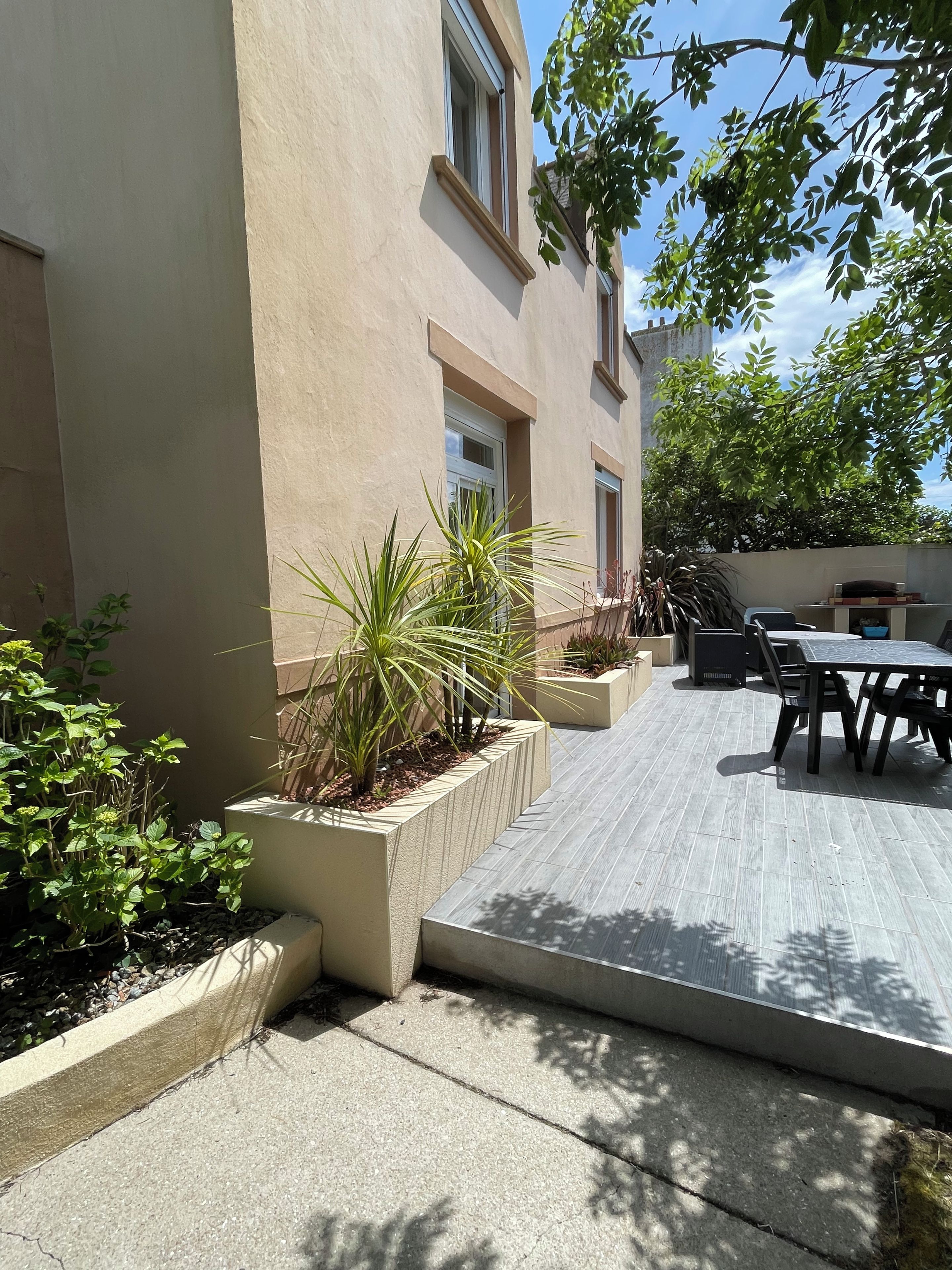 A patio area with outdoor furniture, planters with various plants, and a building with windows and a door.