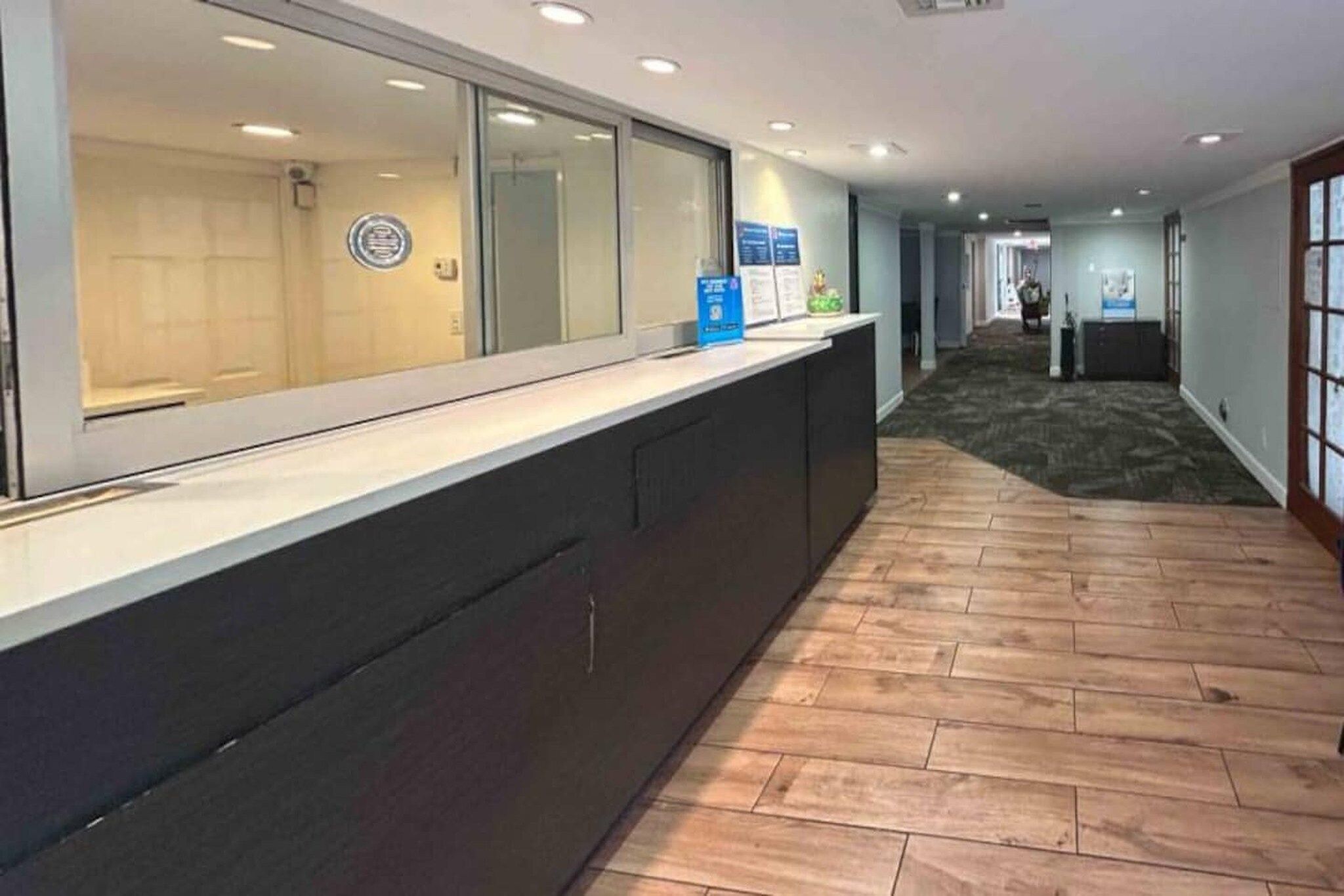 Uma área de recepção com balcão, porta de vidro e corredor com carpete.