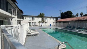 Una piscina con lettini e un edificio sullo sfondo con un balcone.